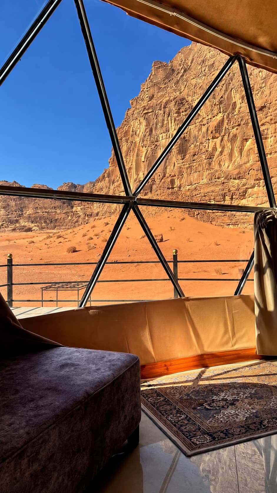 Interior view of a Wadi Rum bubble tent dome looking out through the geodesic glass panels at the red sandstone cliffs and desert landscape