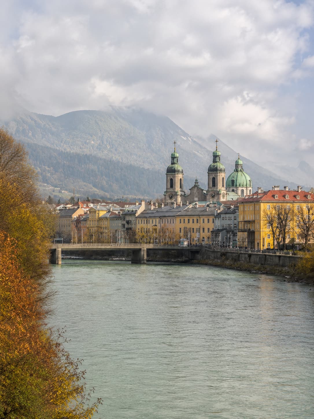 Innsbruck old town Cathedral domes and colourful buildings reflected in the River Inn, with autumn-misted Austrian Alps rising behind in October