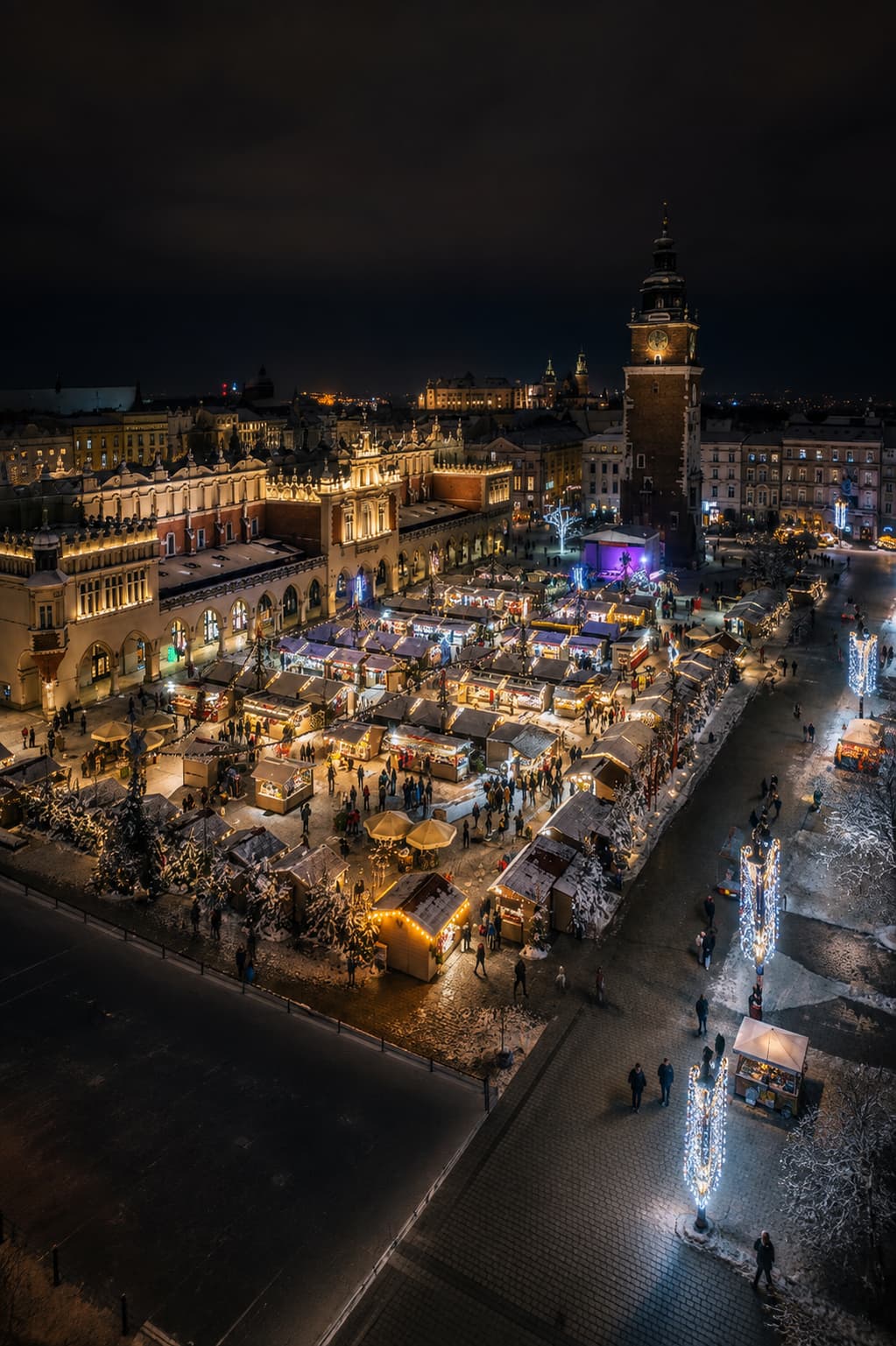 Kraków Rynek Główny Christmas market aerial at night, Cloth Hall and Town Hall Tower illuminated behind stalls