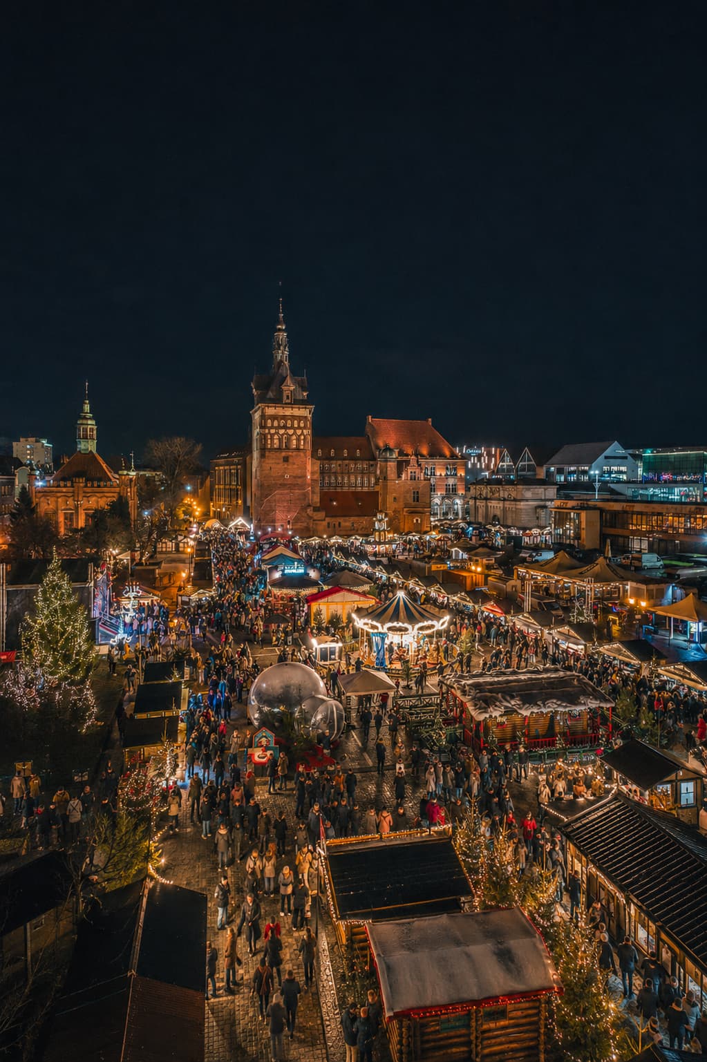 Gdańsk Poland Christmas market aerial at night, Gothic brick tower, carousel and stalls lit along the waterfront