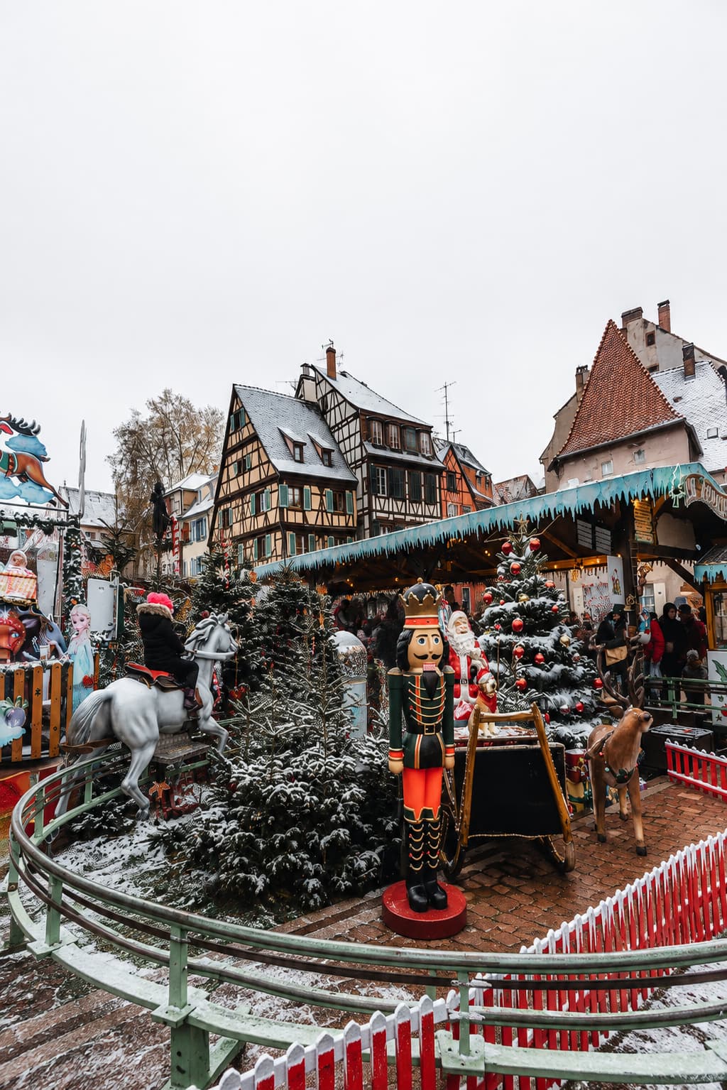 Alsace Christmas market with nutcracker statue, carousel and snow-covered half-timbered buildings