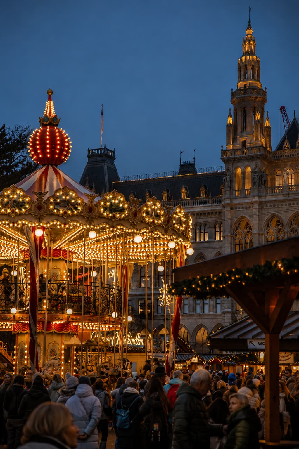 Vienna Rathausplatz Christmas market with ornate lit carousel and Gothic Town Hall behind at blue hour