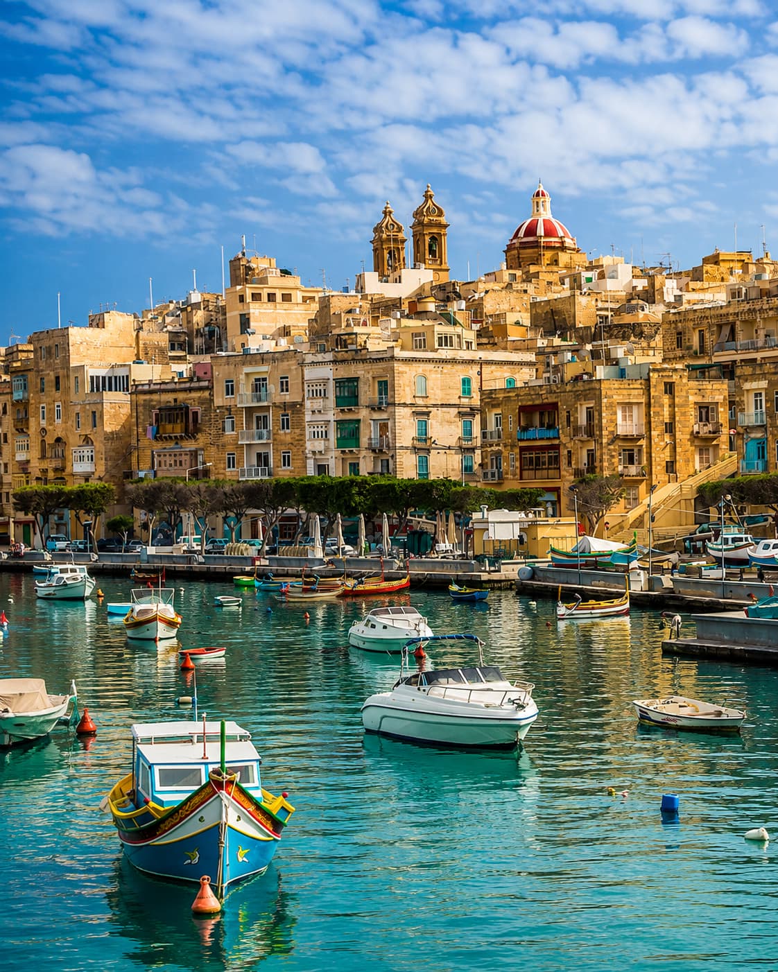 Valletta Malta harbour with traditional colourful luzzu fishing boats on turquoise water and golden limestone buildings rising behind — a quiet birthday trip idea