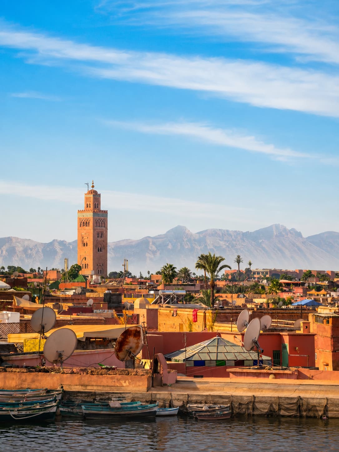 Marrakech rooftop view with Koutoubia mosque minaret rising above the pink medina and the Atlas Mountains visible in the background — a top winter birthday trip idea