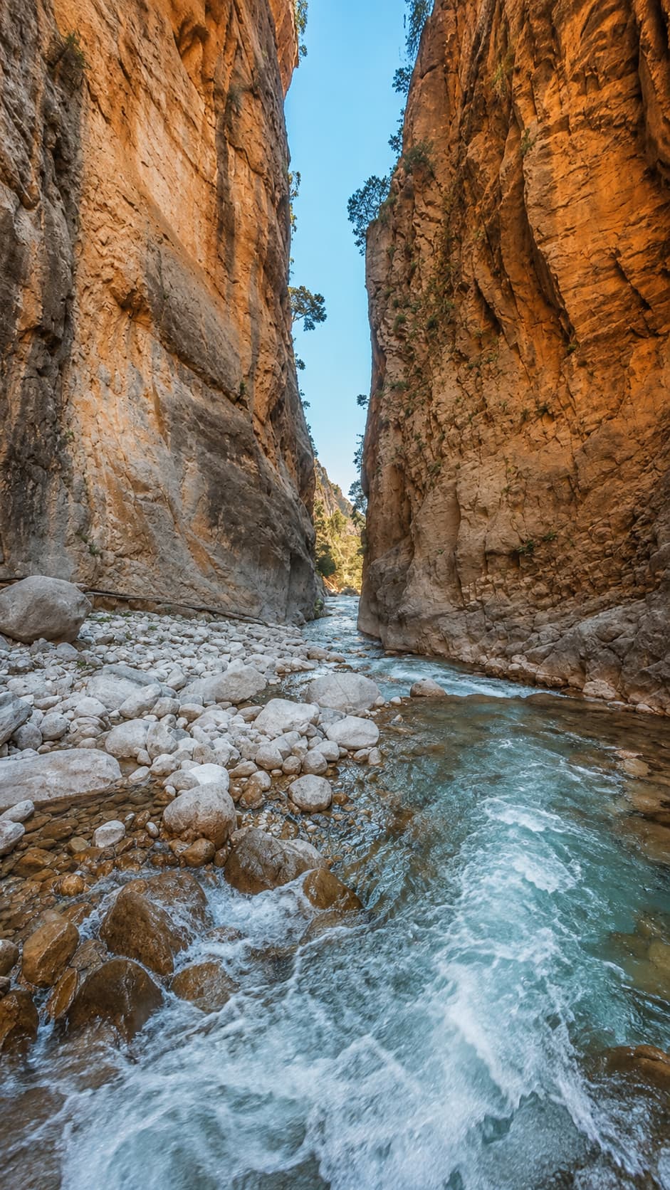 Samaria Gorge Iron Gates in Crete, towering limestone canyon walls with a rushing stream through the rocky riverbed below
