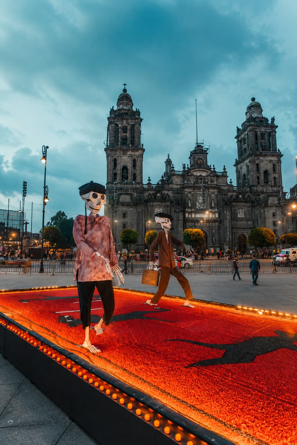 Skeleton figures on illuminated marigold carpet at the Zócalo Day of the Dead installation, Metropolitan Cathedral of Mexico City at dusk