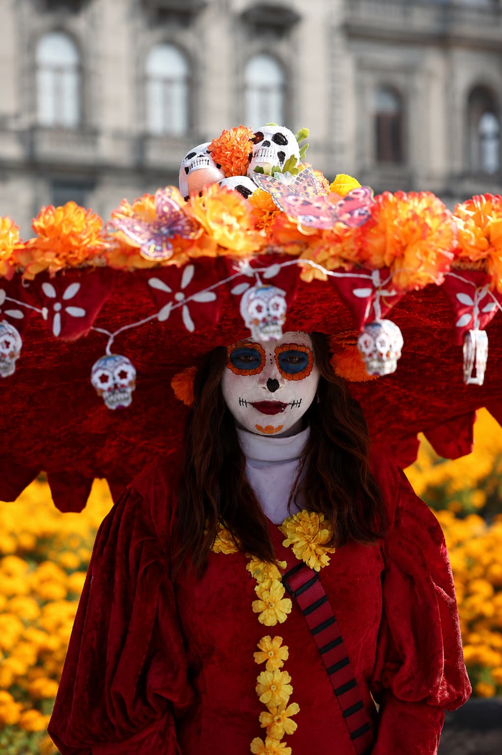Close-up portrait of a Catrina at the Mexico City Day of the Dead parade, elaborate red hat decorated with marigolds and sugar skulls