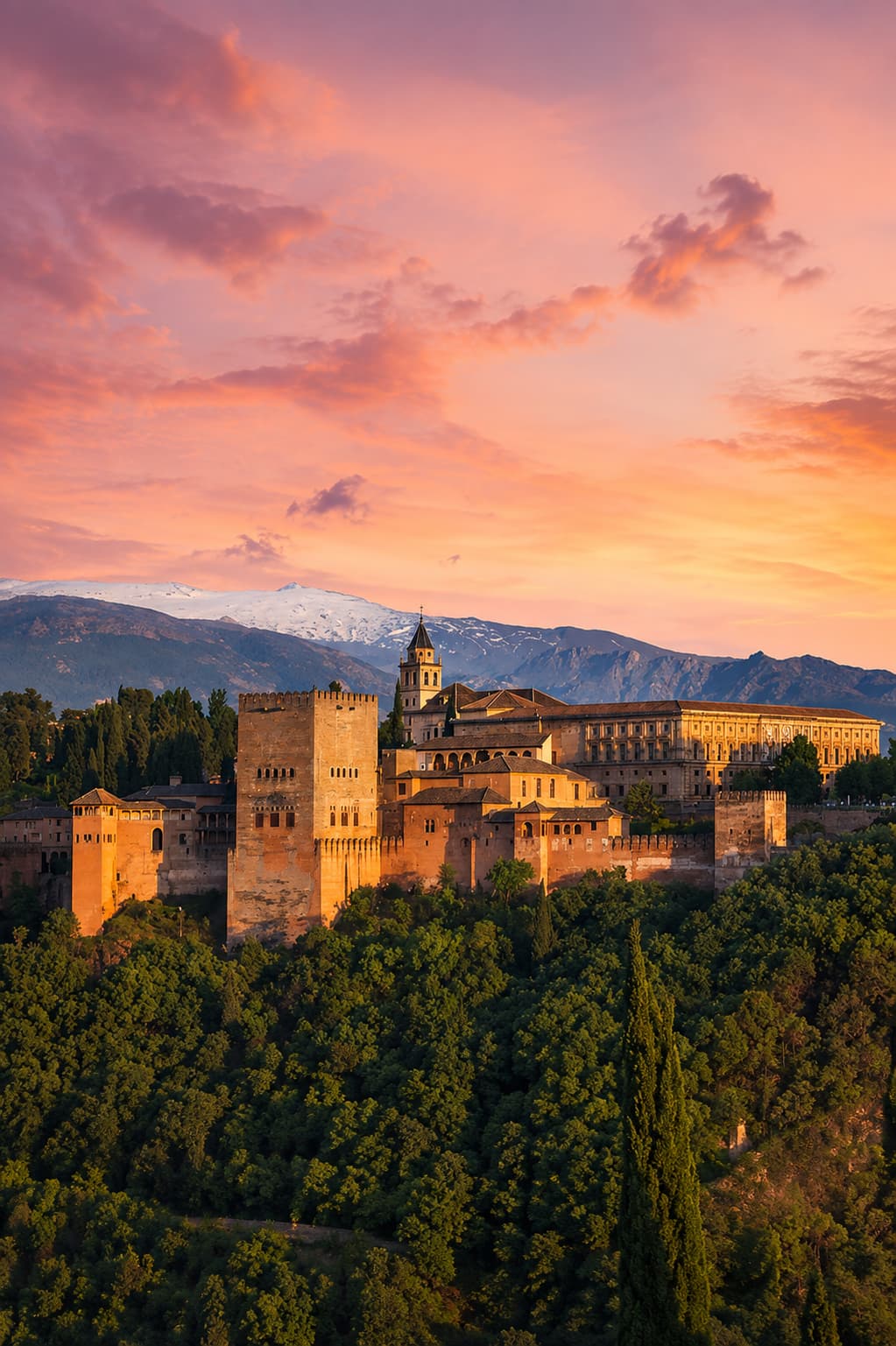 The Alhambra palace in Granada Spain at dramatic pink sunset with snow-capped Sierra Nevada — warm December destination in Andalusia