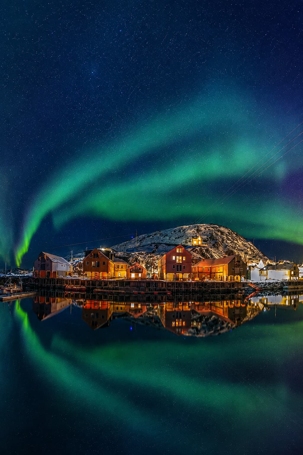 Vivid green northern lights arching over a Norwegian fishing village and reflected in still harbour water — northern Norway is one of the most dramatic European destinations in November for aurora season