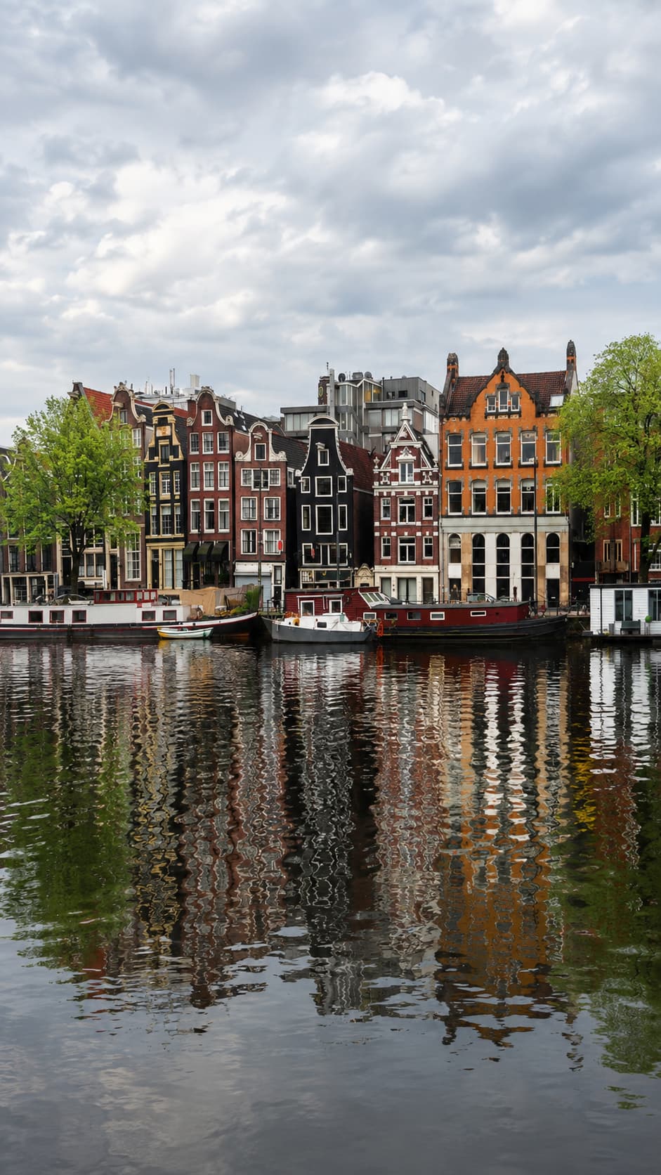Classic Amsterdam canal houses with gabled facades reflected in still water — Amsterdam is one of the best European city destinations in November