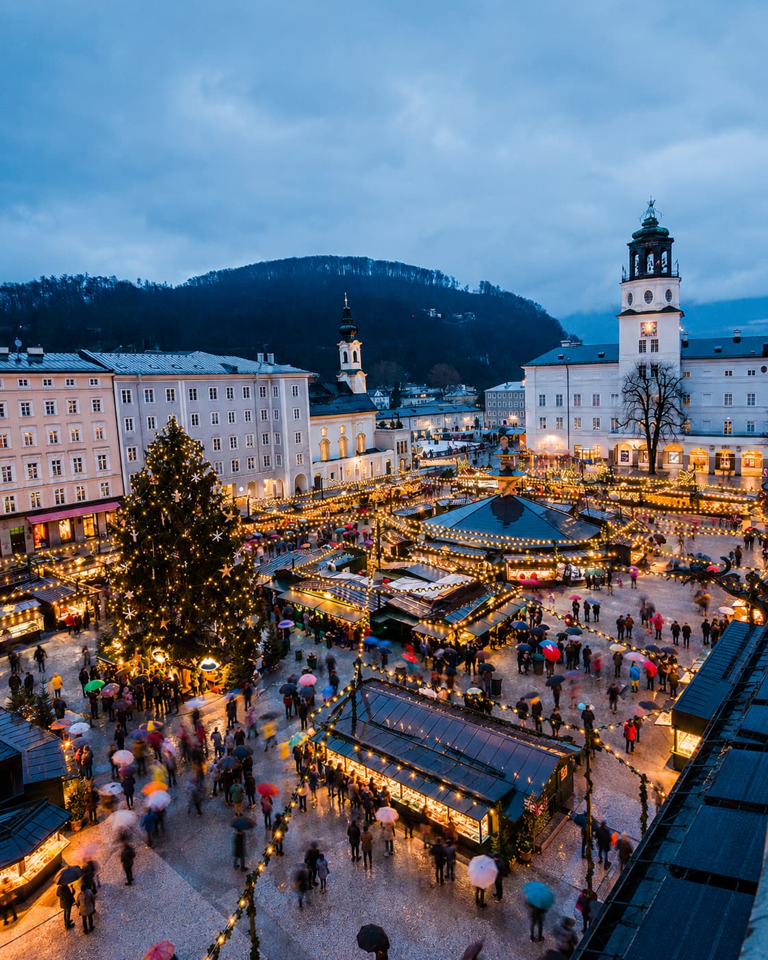 austria christmas markets — Salzburg Christkindlmarkt from above at dusk, golden lights and church tower, hillside behind