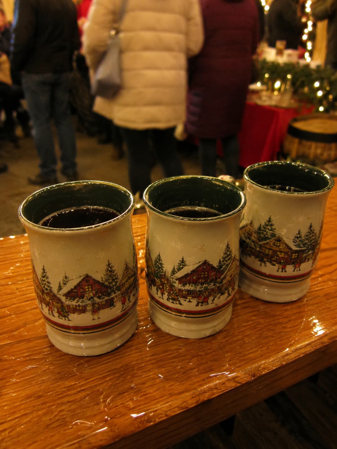 Glühwein ceramic mugs at a german christmas market counter, festive village scenes painted on white cups