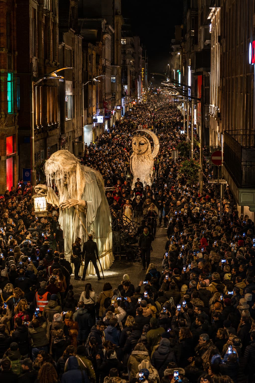 Massive Halloween street parade in a European city at night, giant ghost and owl puppet figures moving through tens of thousands of spectators lining both sides