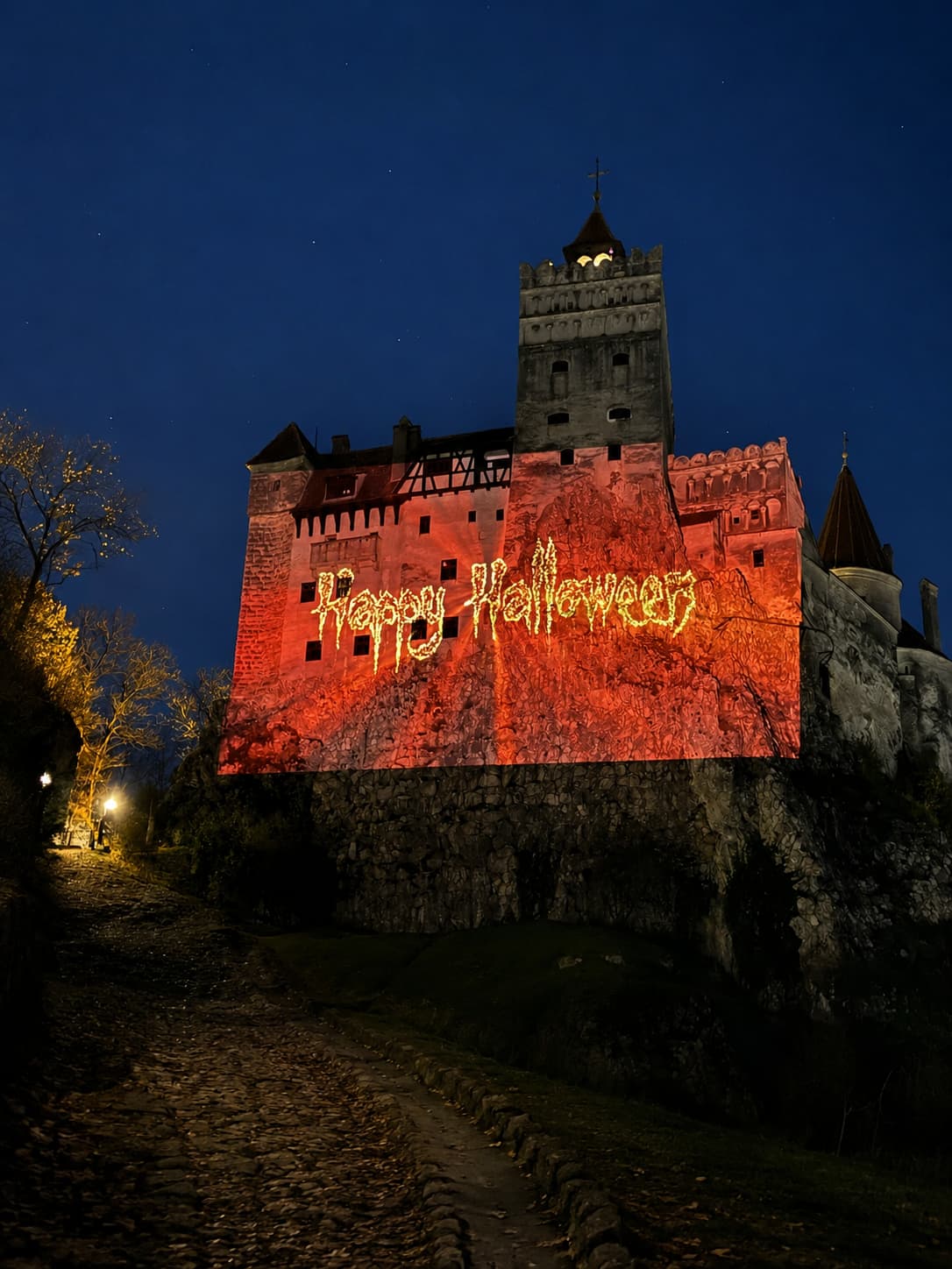 Bran Castle in Transylvania at night with Happy Halloween projected in glowing orange letters across the medieval stone walls