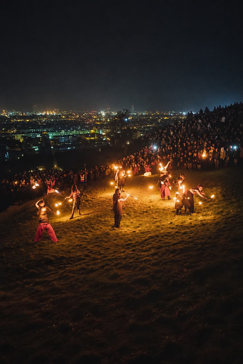 Samhuinn Fire Festival on Calton Hill Edinburgh at night, fire performers scattered across the hillside with the city lights glowing below and a huge crowd watching