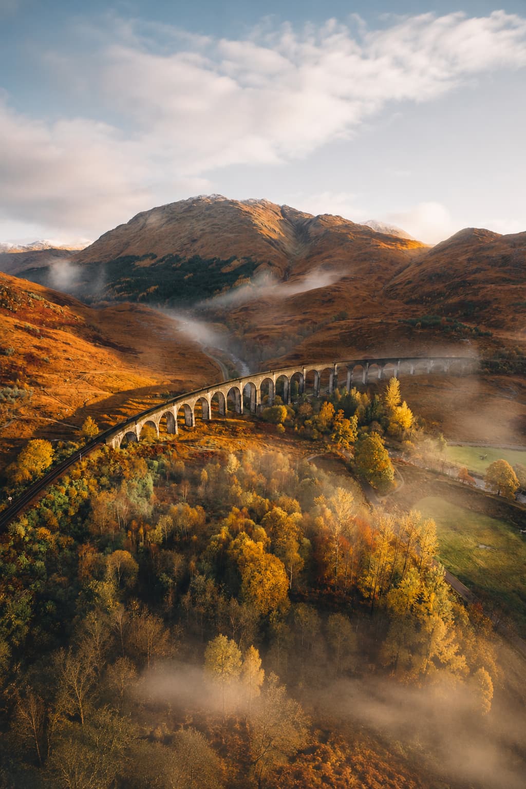 Glenfinnan Viaduct in the Scottish Highlands in autumn with morning mist in the valley, golden trees and moody low cloud on the hillsides