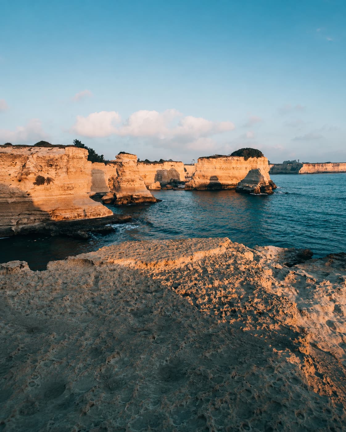 Pale limestone sea cliffs catching warm sunset light along the Puglia Adriatic coast, calm blue sea visible below