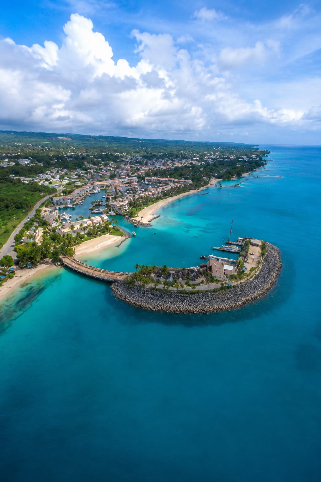Aerial view of a Caribbean coastal town with a curved stone breakwater and turquoise harbour — a short-haul international destination for US East Coast travelers at Thanksgiving