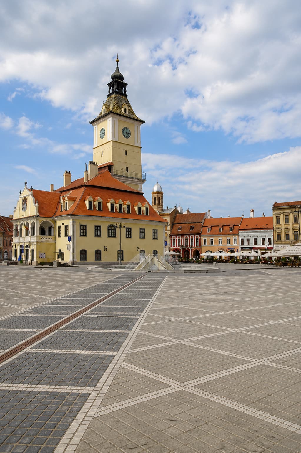 Brașov Council Square (Piața Sfatului) — the old Council House with clock tower and red-tiled roof, pastel merchant buildings lining the medieval Saxon square in Transylvania
