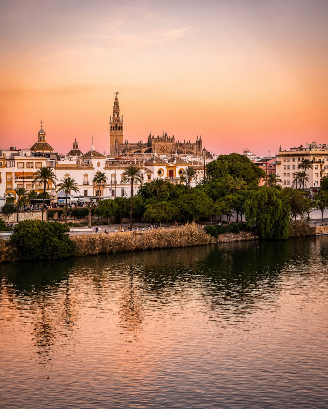Seville's Giralda tower and cathedral silhouetted at sunset over the Guadalquivir river — Andalusia in autumn at golden hour