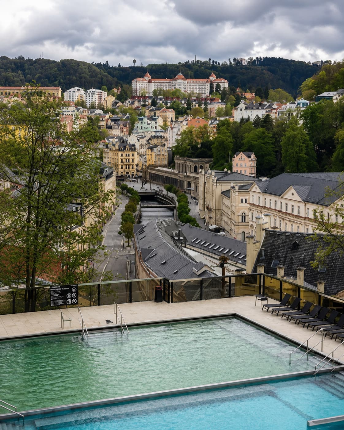 Rooftop thermal pool overlooking the Belle Époque townscape of Karlovy Vary, Czech Republic — one of the best spa towns in Europe — with forested hillsides rising behind the colonnaded promenade