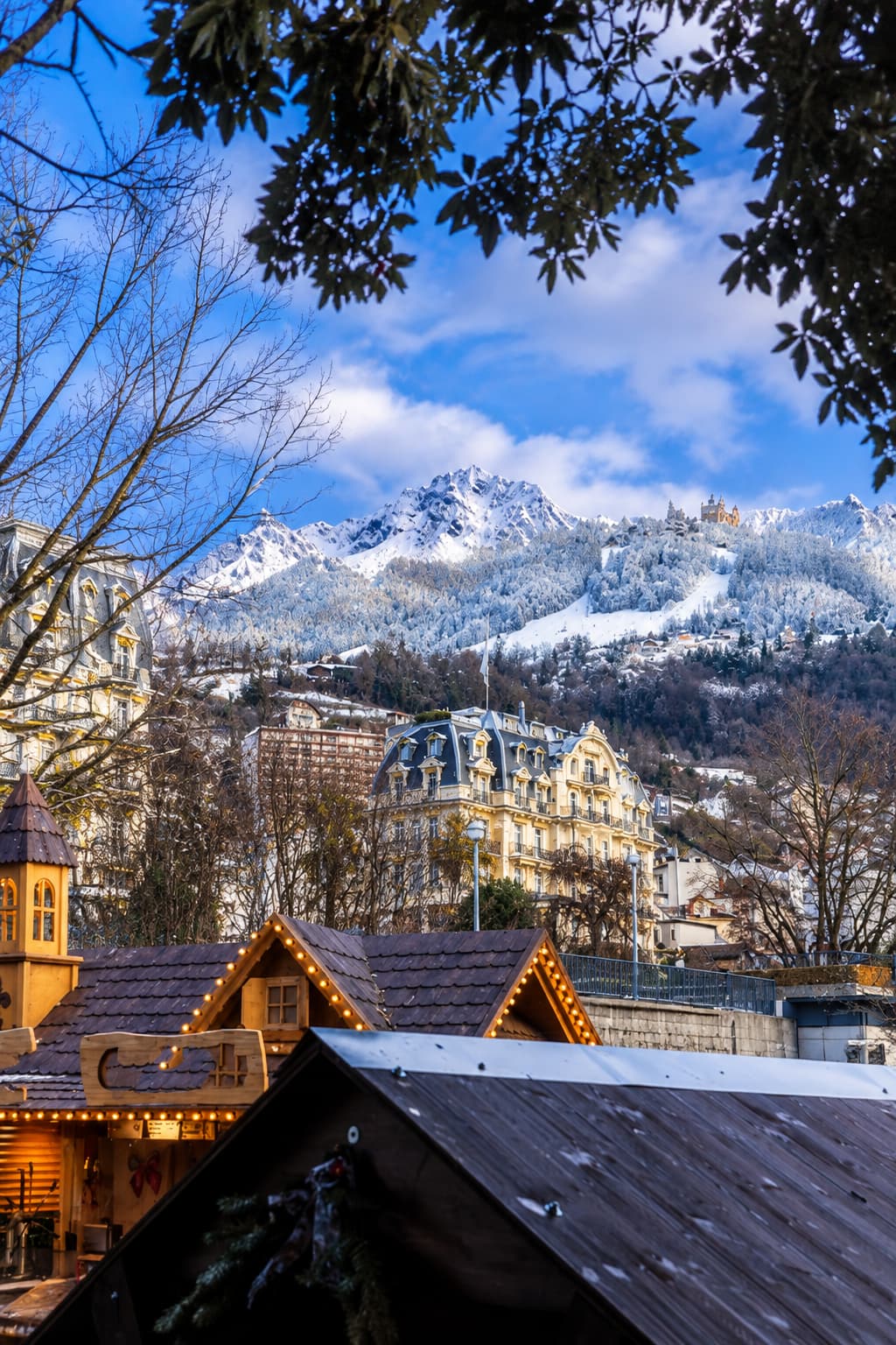 Montreux Christmas market wooden chalets with their rooftop lights glowing beneath a snow-dusted Alpine peak and a Belle Époque hotel, Montreux Riviera
