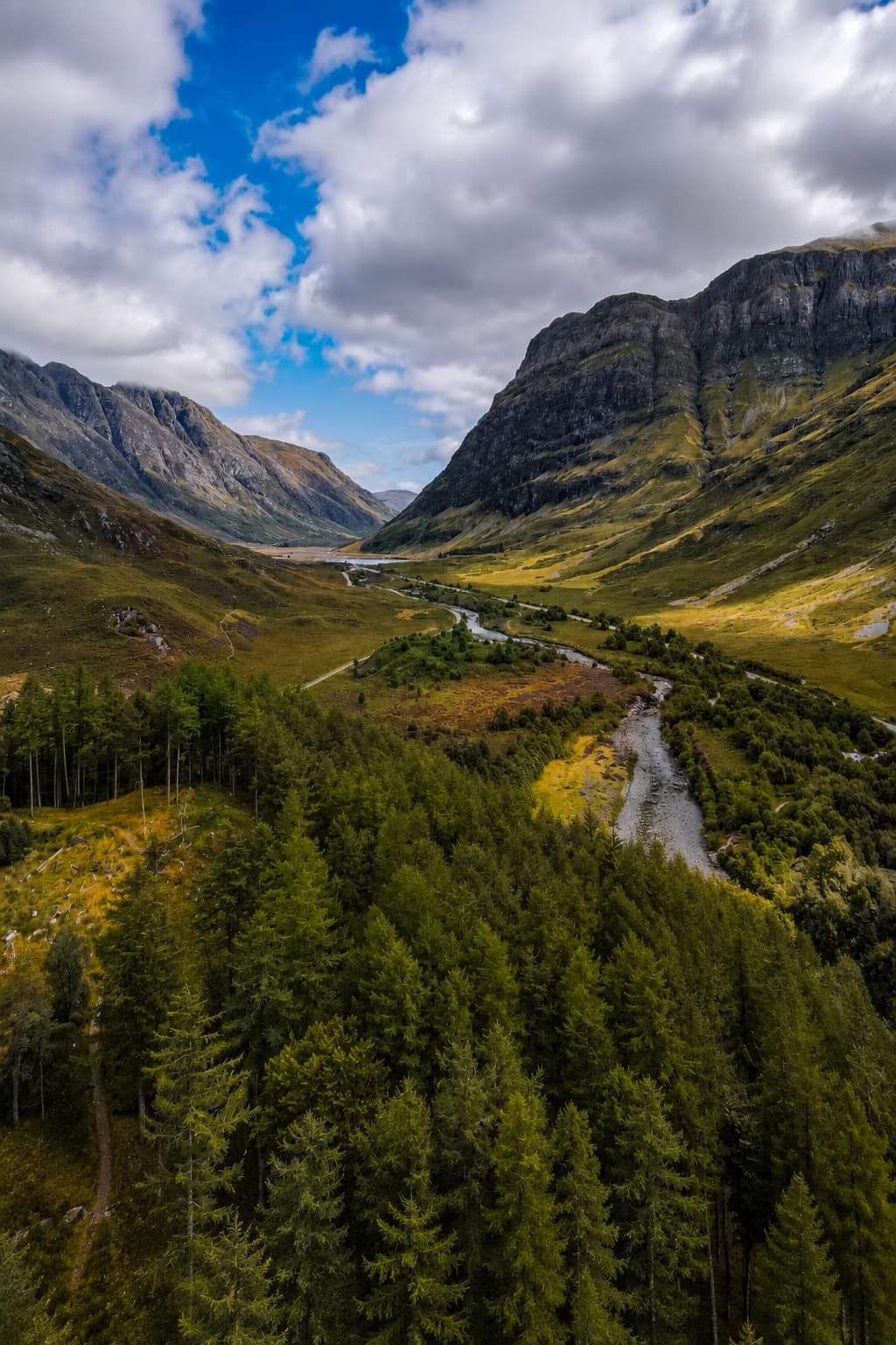Aerial view of Glencoe valley, winding river and conifer forest on the valley floor, steep mountain walls rising on both sides
