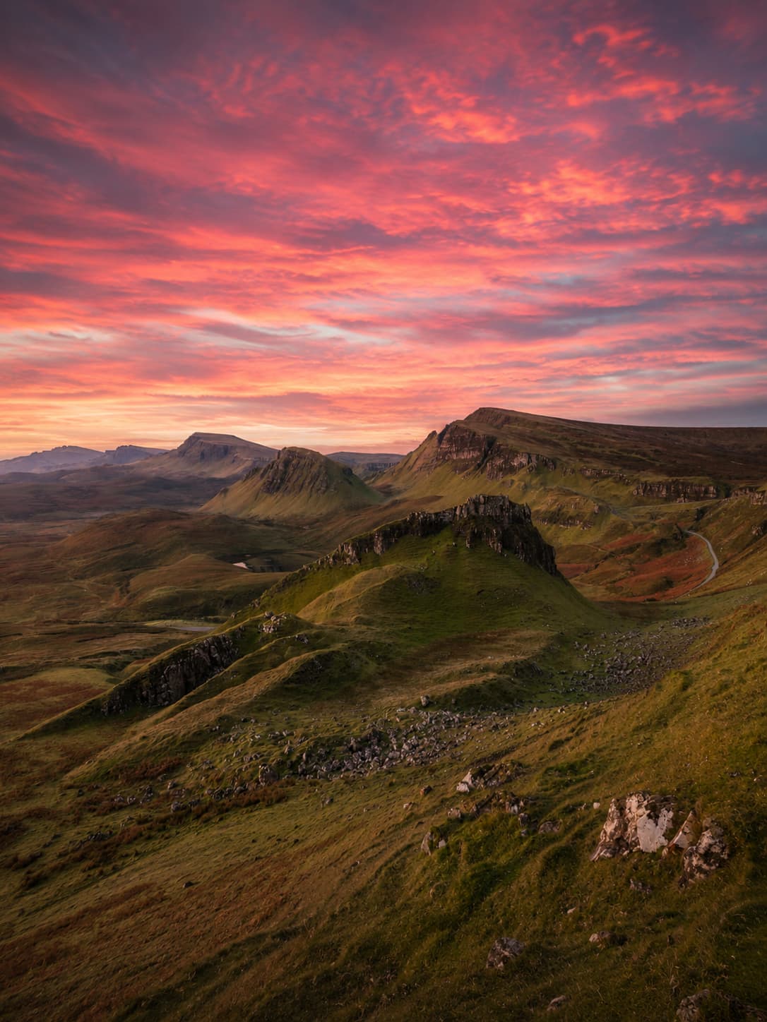 The Quiraing on the Isle of Skye at sunrise with a vivid crimson and pink sky over the rugged green ridgeline in October