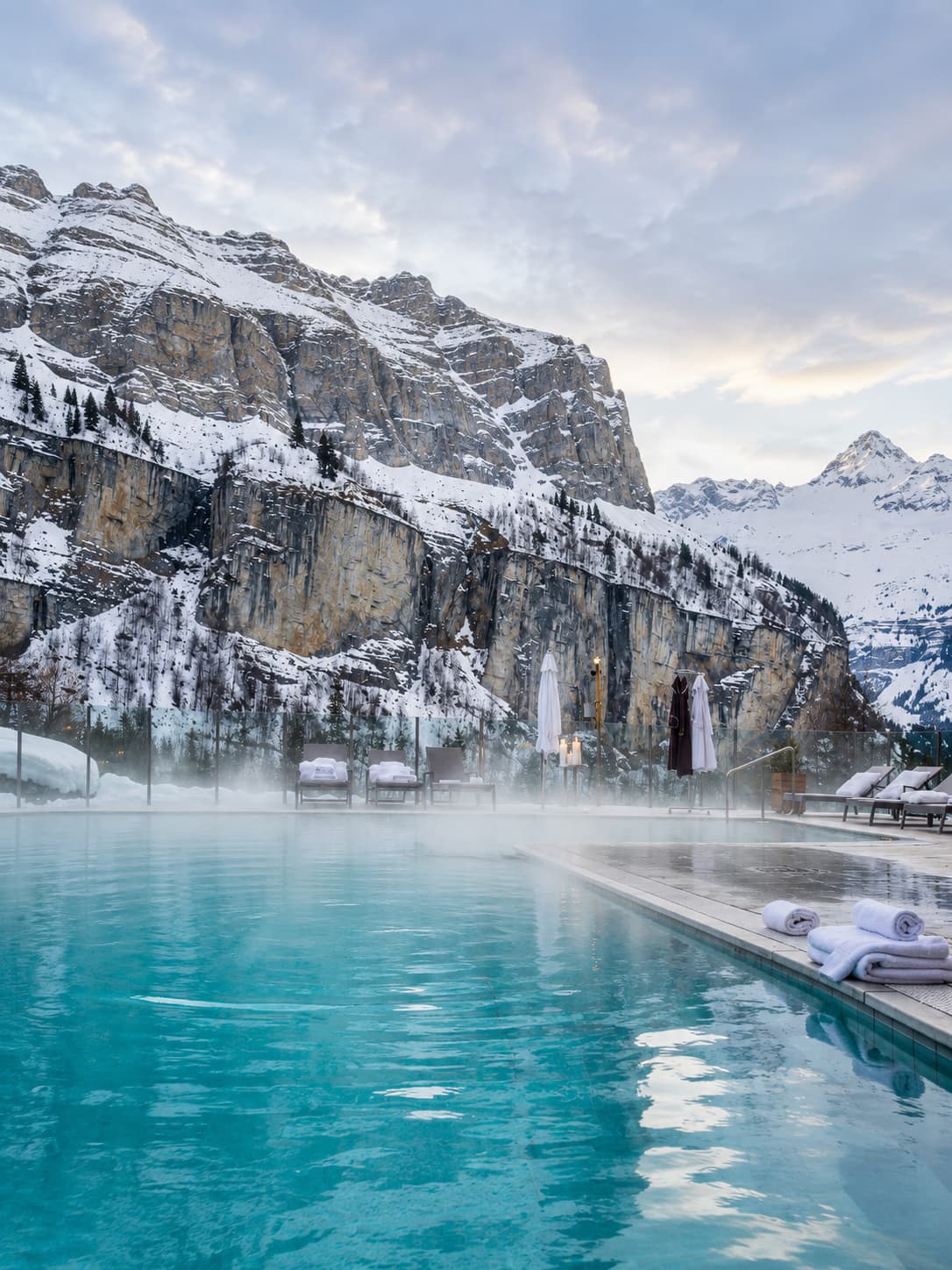 Outdoor thermal infinity pool with steam rising, surrounded by snow-covered limestone cliffs — the defining experience of Switzerland in winter without skiing at Leukerbad